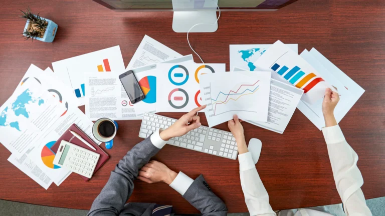 Two business professionals reviewing colorful charts, graphs and financial reports on a desk