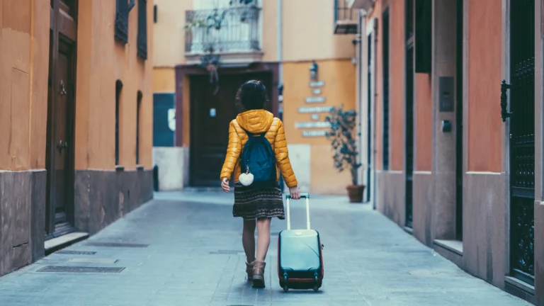 Person with rolling suitcase walking down a narrow street in Spain after arrival