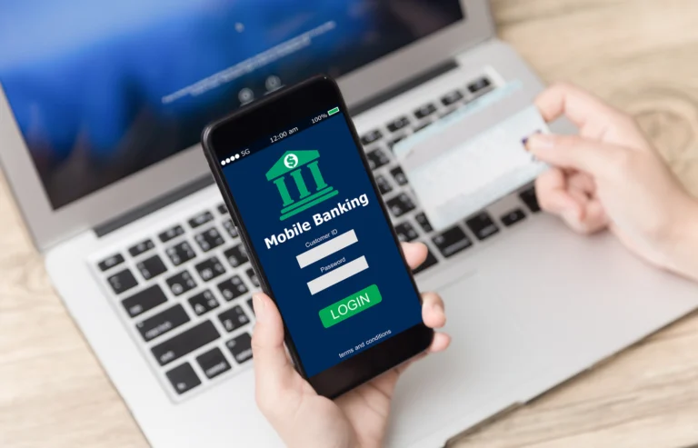 Person using a mobile banking app on a smartphone with a credit card and laptop nearby